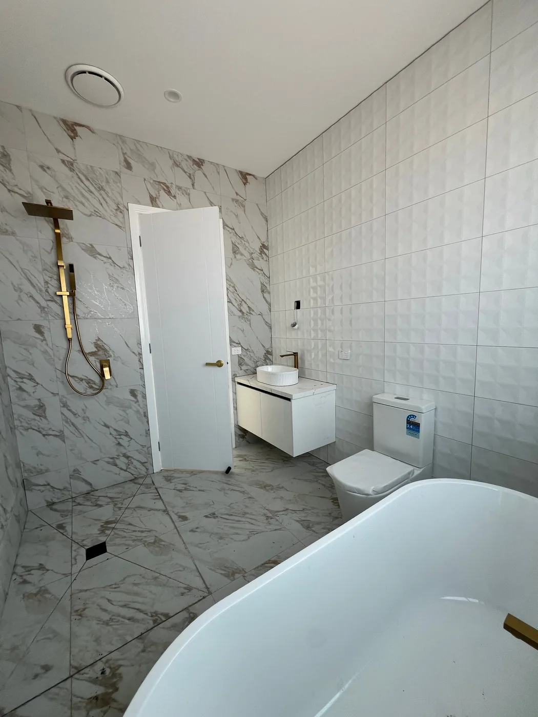 Marble bathroom with installed basin, gold shower fittings, toilet and freestanding bath