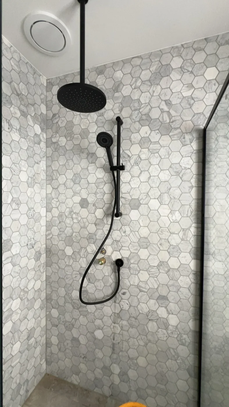 Black overhead and handheld shower fittings against hexagonal tiles